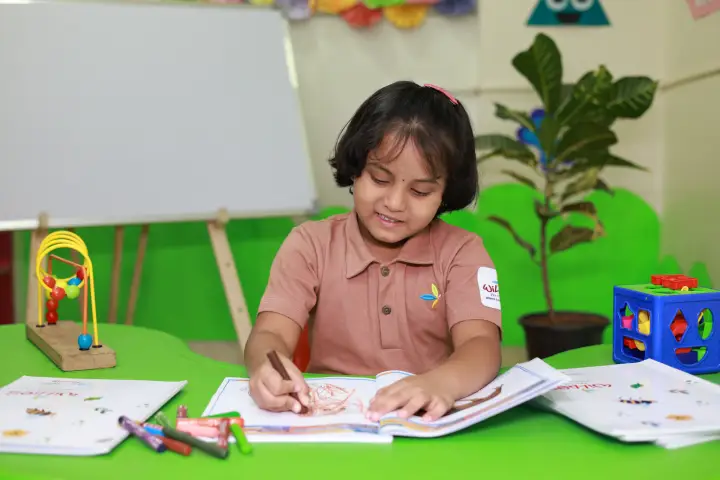 Girl in Williez uniform writing in a notebook at a classroom desk