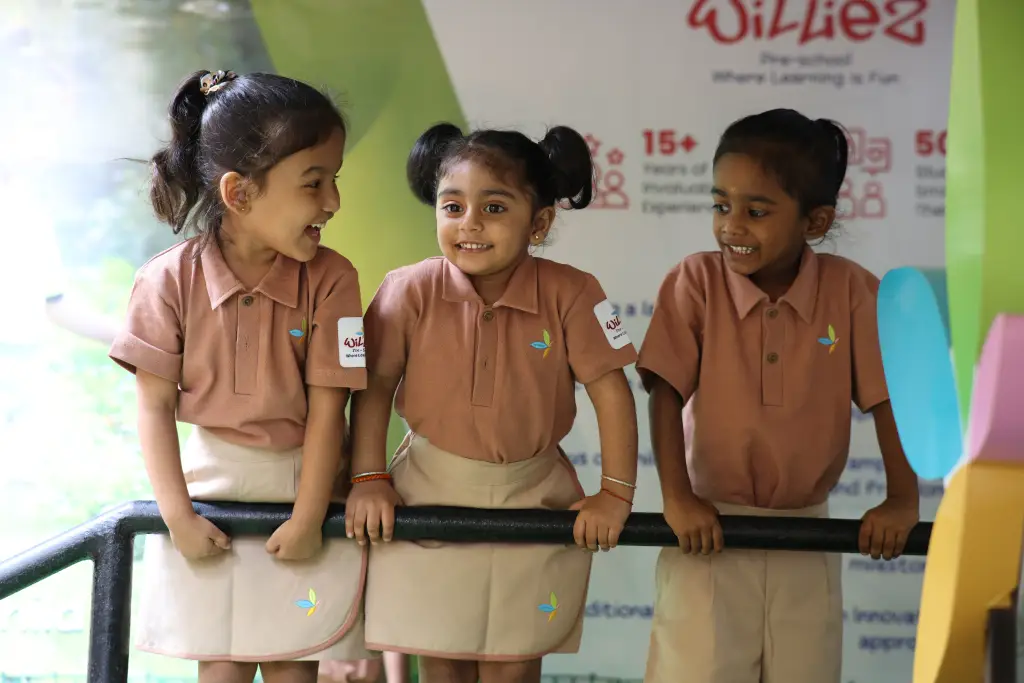 Three smiling children in Williez uniform standing together in class