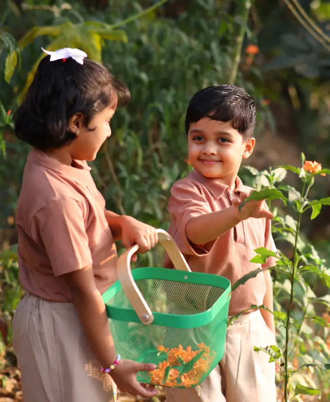 Two children picking leaves into a basket during an outdoor gardening activity