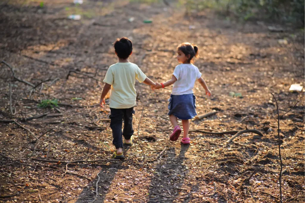 Two young children walking hand in hand along a forest path