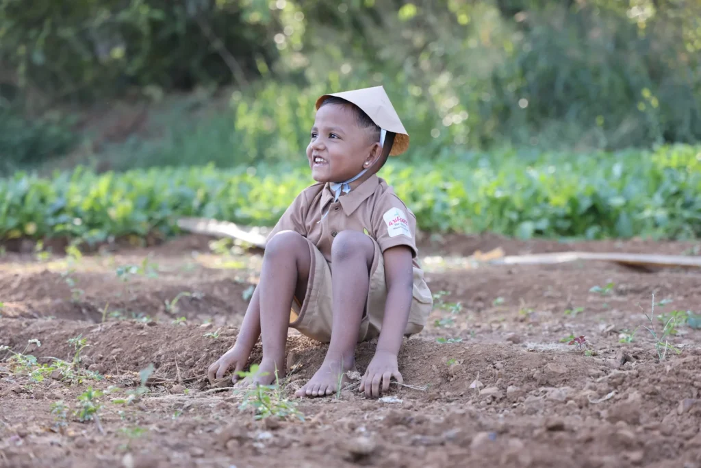 Smiling boy sitting in the field during a farm visit at Williez Preschool, India