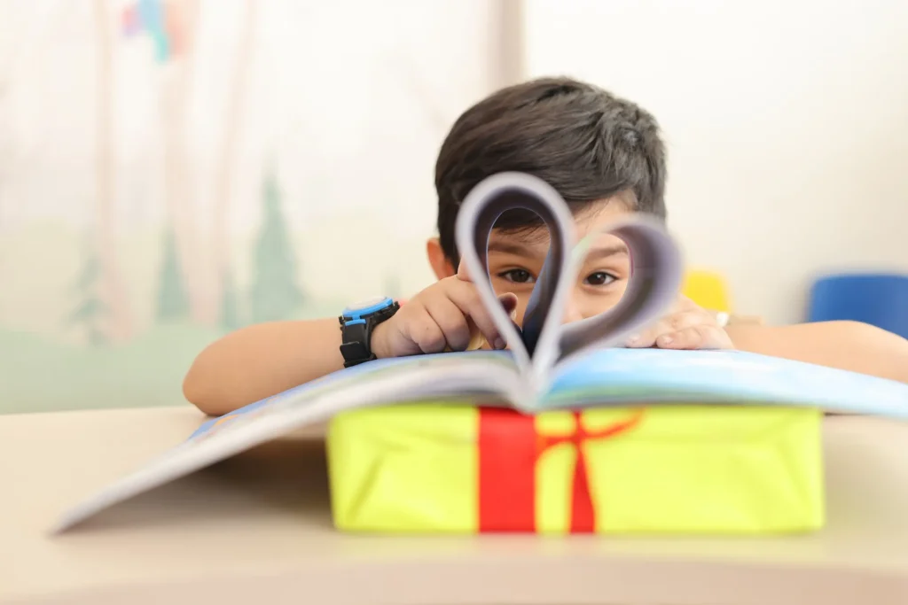 Boy holding a book folded into a heart, showing a love of reading at Williez Preschool, India