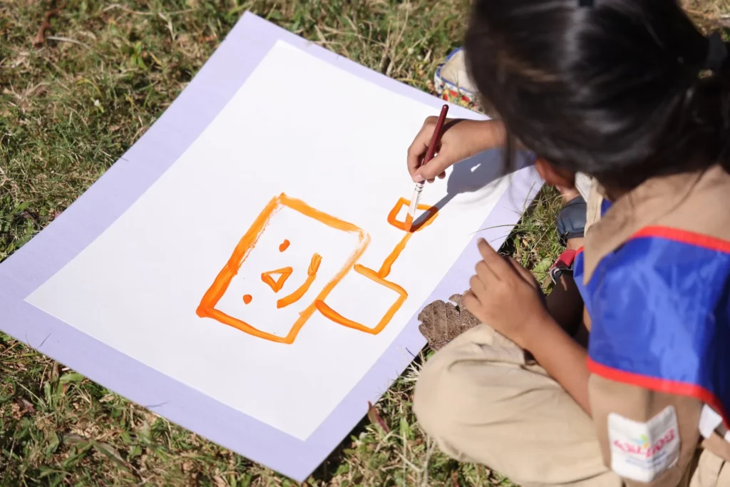 Child painting on paper during an outdoor art session at Williez Preschool, India