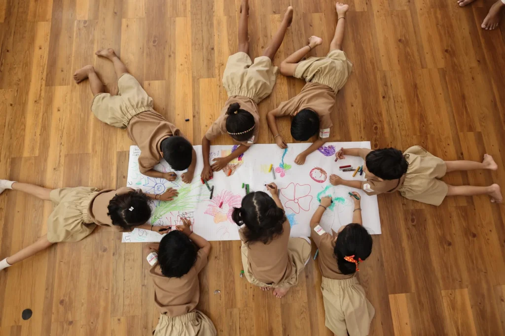 Children drawing together on a large sheet of paper at Williez Preschool, India