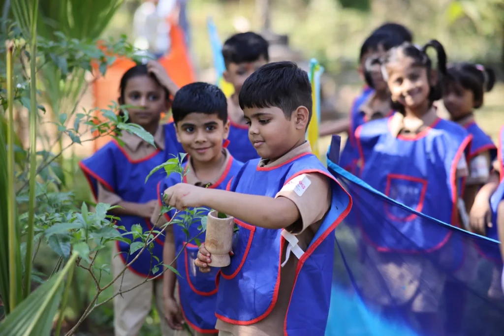 Children in aprons planting saplings together at Williez Preschool, India