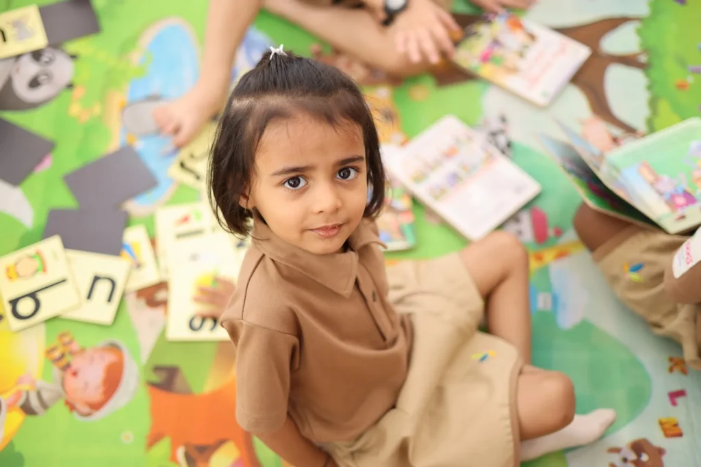 Little girl enjoying picture books during reading time at Williez Preschool, India